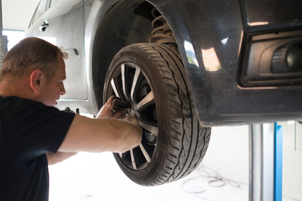 Mechanic performing a vehicle inspection by removing a car wheel for maintenance.
